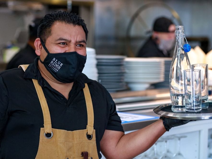 Picture of man carrying tray of water with a mask on