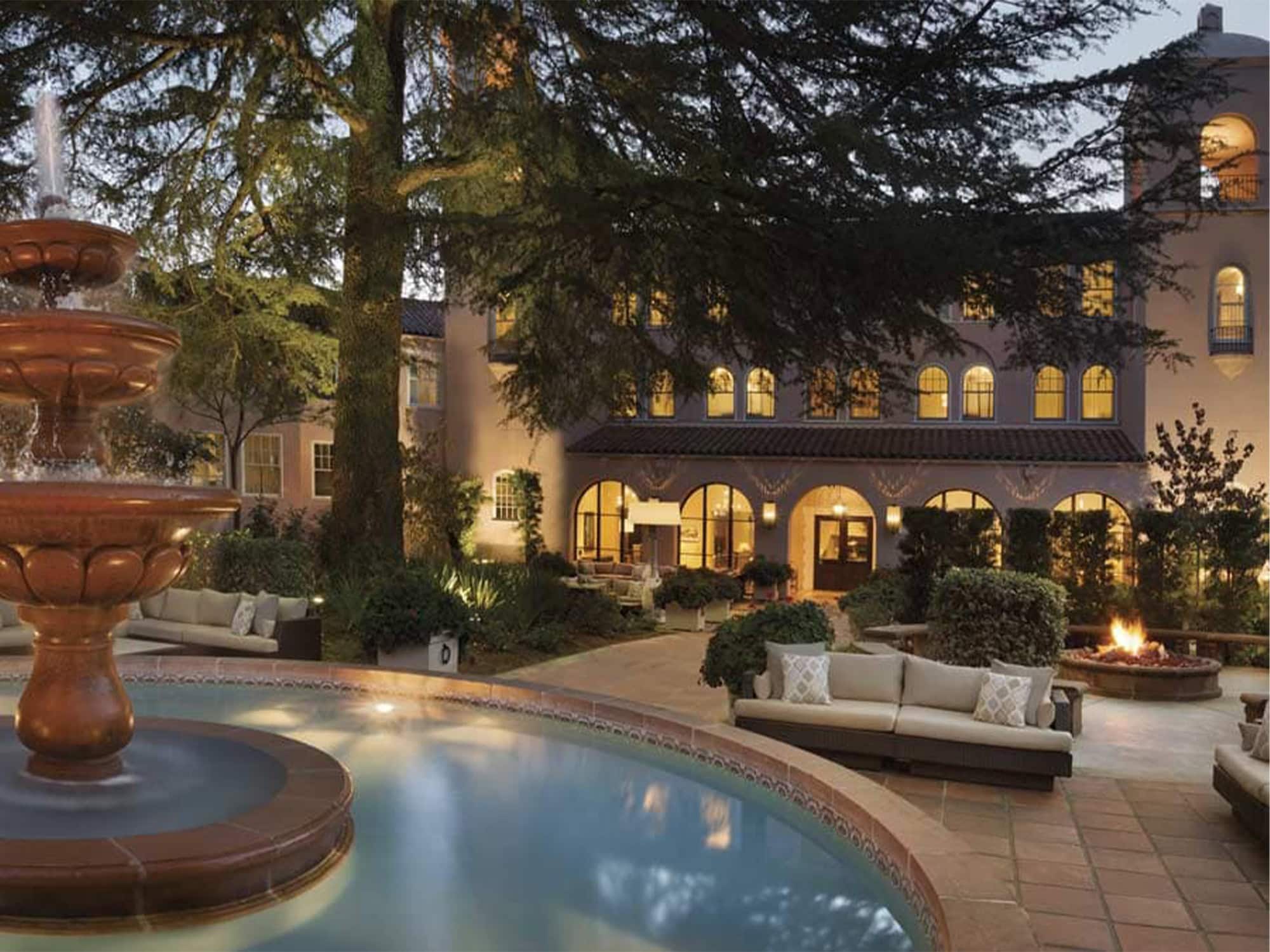 A fountain and a pool outside of the hotel is surrounded by palm trees