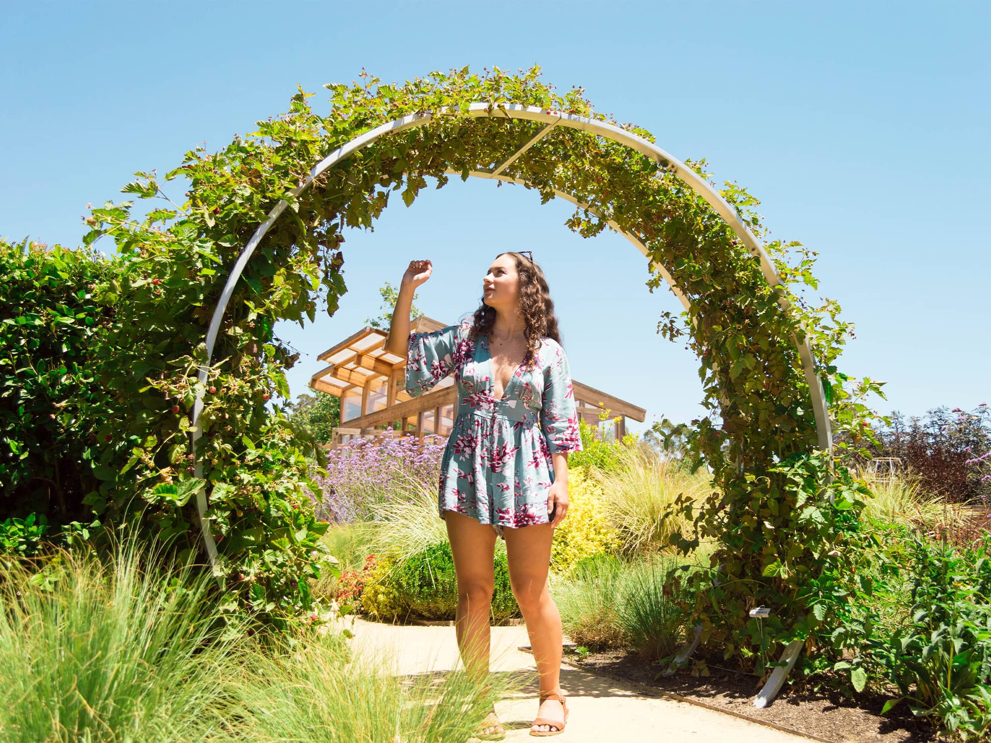 A woman poses for a photo under an arbor of flowers