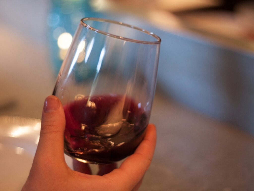 holding up a glass of red wine with a gold rim