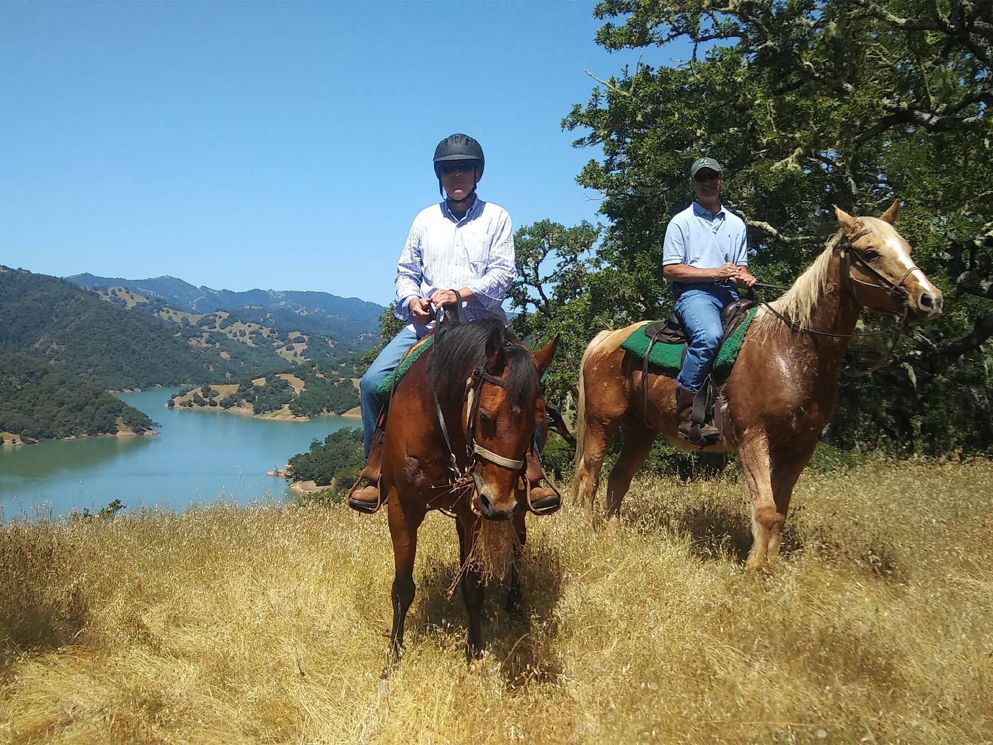 Two people riding horses pose in front of the lake below