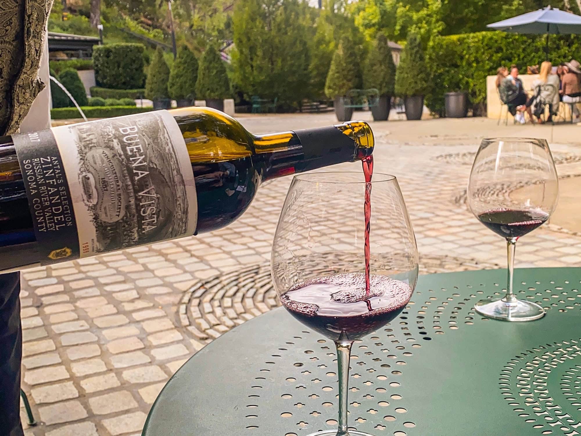 A glass of red wine being poured in a historic courtyard