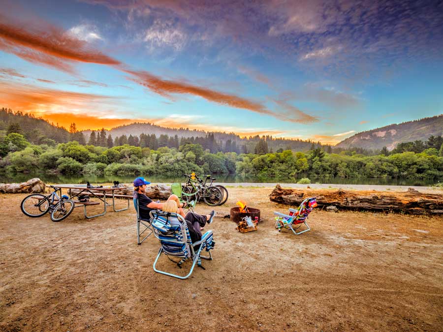 People sit around a fire pit while the sun sets behind them at Casini Ranch Family Campground, Sonoma County