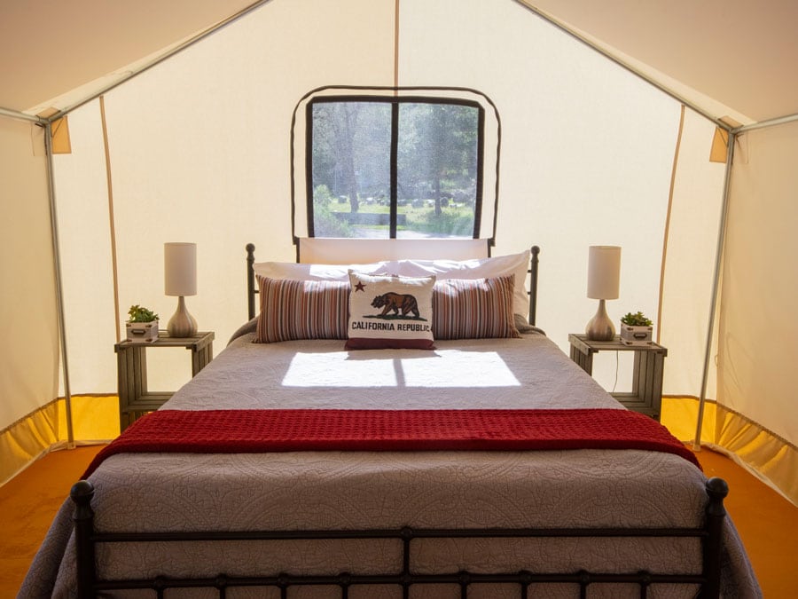 The interior of a glamping tent has a comfy bed with a pillow that has the bear Flag on it in Sonoma County