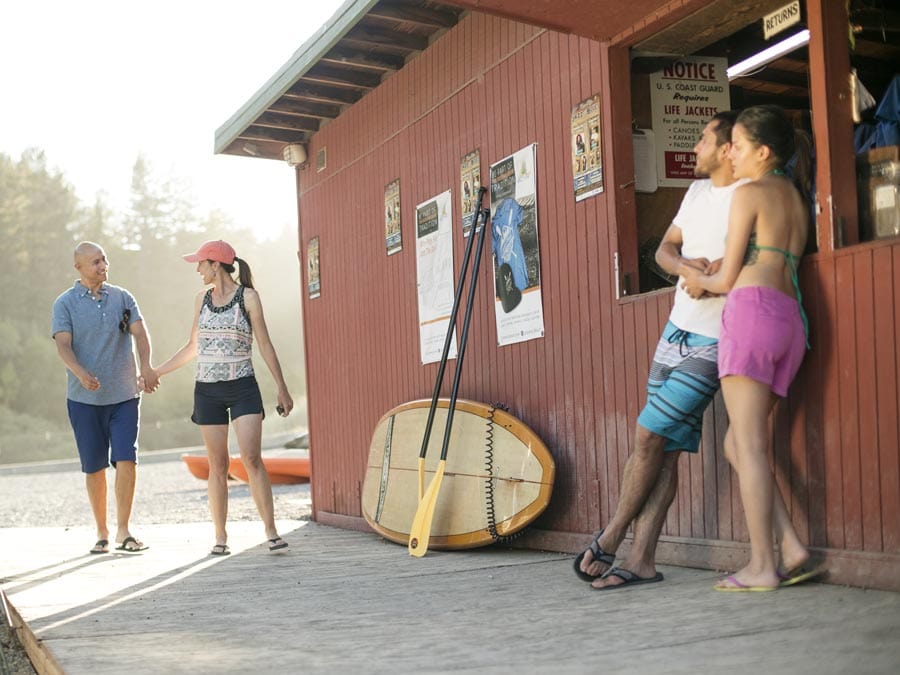 People walk by the building where you rent paddle boards on the river beach