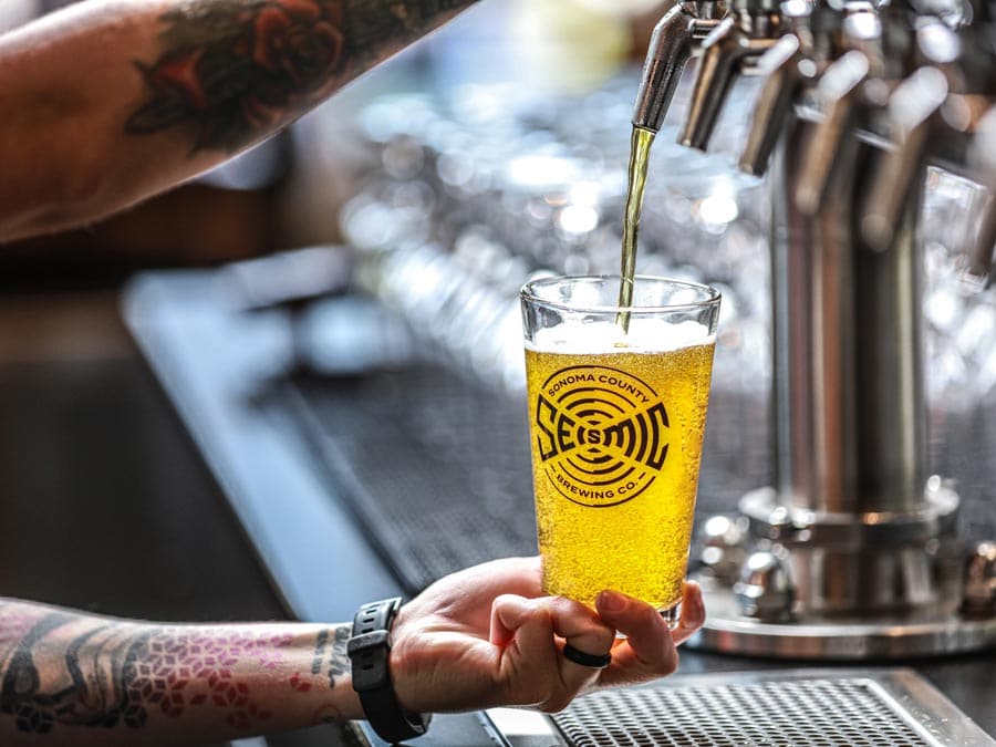 A person with tattoos on their arm pours a beer from a tap