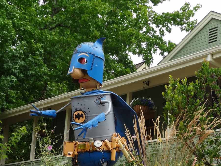 A metal sculpture of Bat Man in front of a house