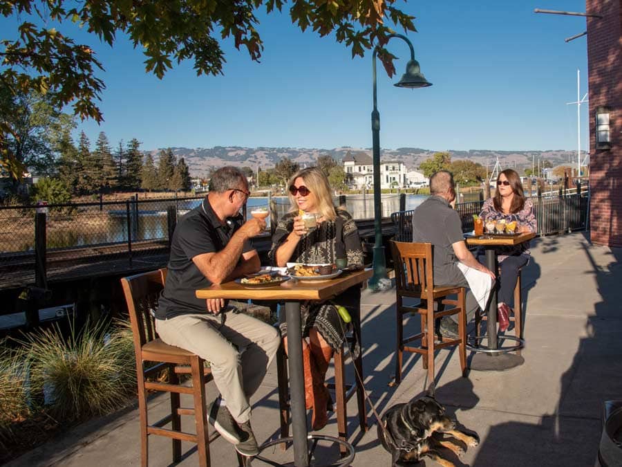 People sit at high top tables along the river