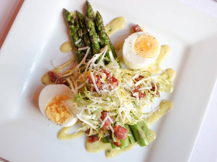 A plate with asparagus spears, hard boiled eggs and a sauce