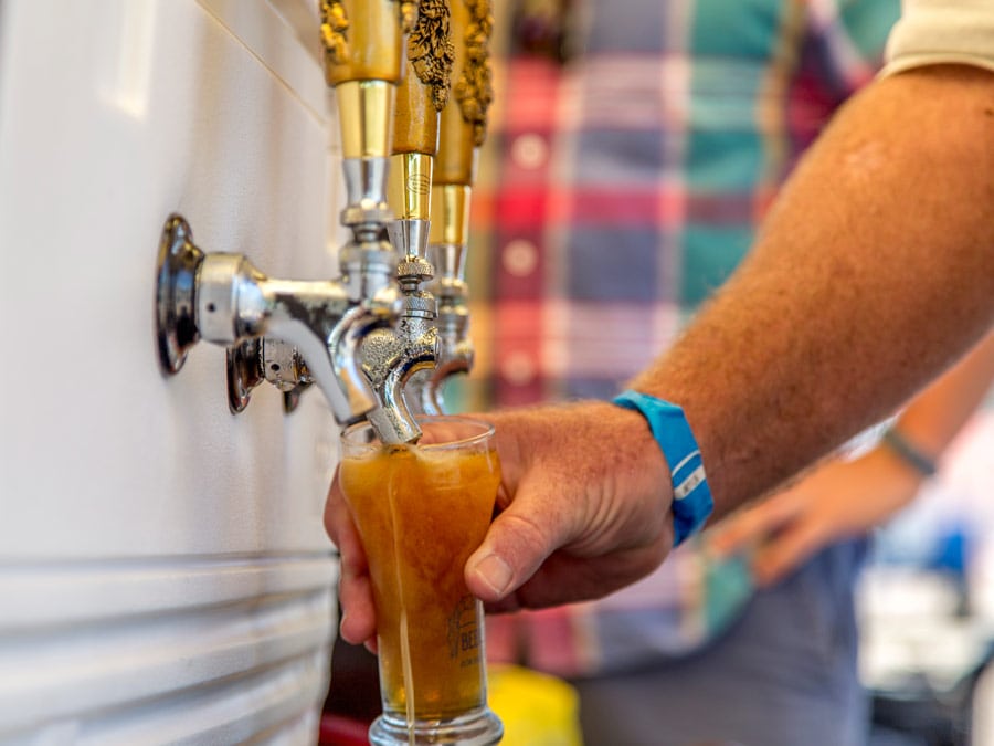 A person pours a beer out of a cooler at a festival