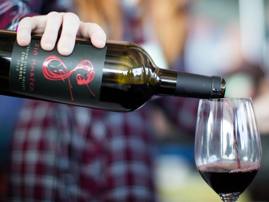 The hand of a person pours red wine into a glass