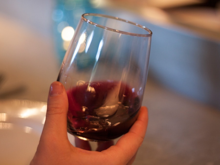 A hand holds a stemless glass of red wine