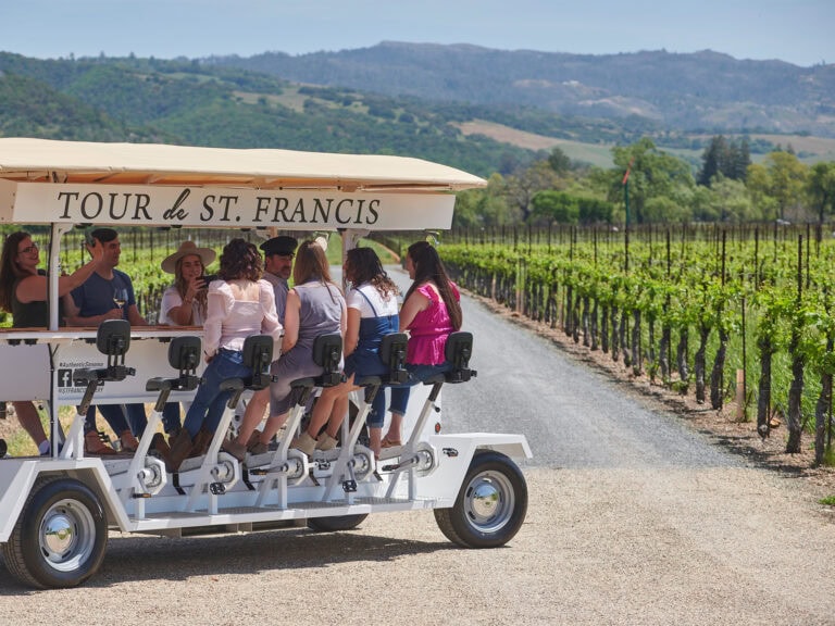 Group of women and one man on a trolley riding through the vineyards at St. Francis.