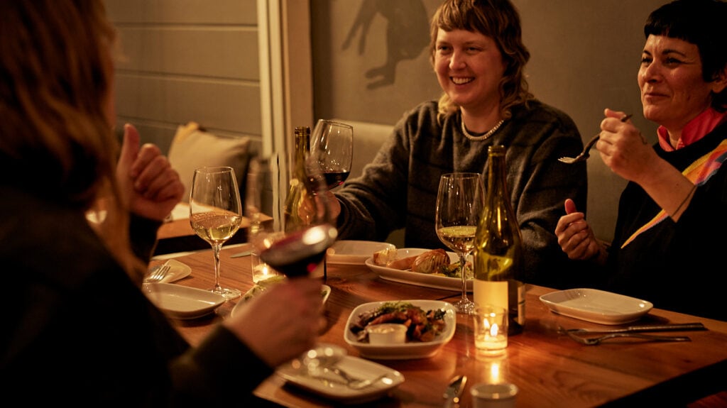 Three people enjoying food and wine at restaurant table.