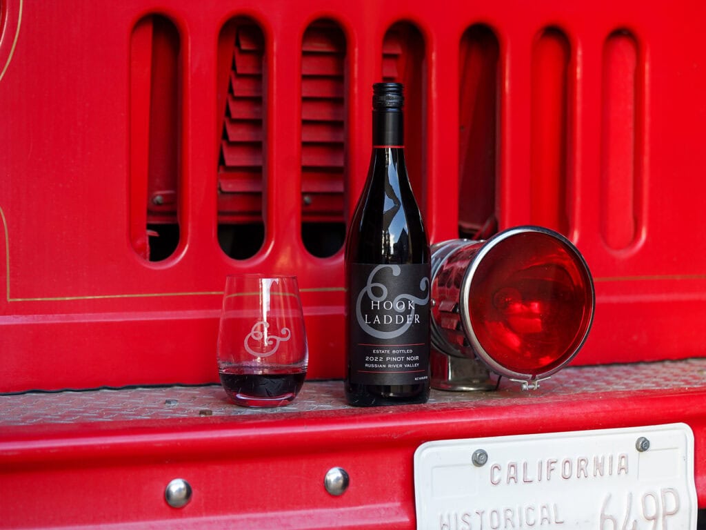 a glass and bottle of hook and ladder pinot noir against a fire truck