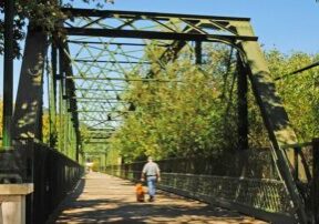 Man and dog walking across steal bridge