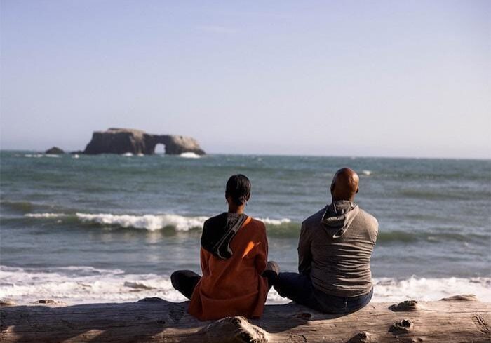 Couple sitting on the beach by the water with legs crossed